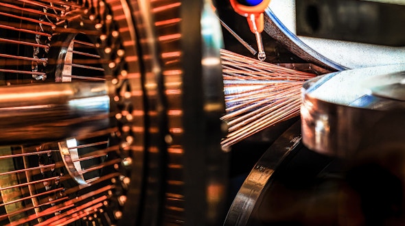 Close-up of the interior of a scientific machine. On the left, a circular arrangement of evenly spaced copper-colored rods radiates outward from a central hub. The bundle of thin copper wires converges on the right into a silver cylindrical component.