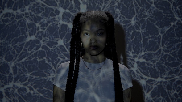 Woman with braids standing in front of a projection of cosmos.