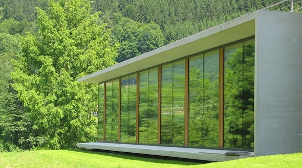 A photo of the north side library extension at the Mathematisches Forschungsinstitut Oberwolfach (MFO, Oberwolfach Research Institute for Mathematics) showing a mostly glass building in a green landscape.