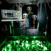 Photo of glowing green tabletop laser equipment with researchers looking on.