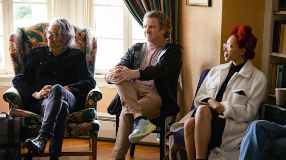 Three people sitting on chairs in and part of group discussion.
