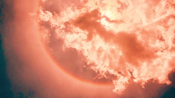 Still image from Absolute Zero: A full moon partially obscured by dramatic, billowing clouds, bathed in deep coral and orange hues, creating an ethereal and moody atmosphere.