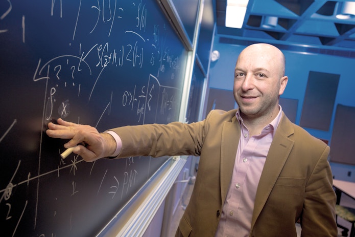 Portrait of Alex Kontorovich writing on a blackboard.