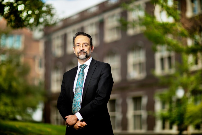 A portrait of Robert Ghrist in a suit, standing outside a brick building.