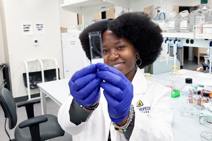 A photo of Florence Njoroge in the lab, holding a slide containing 10-µm zebra finch brain sections.