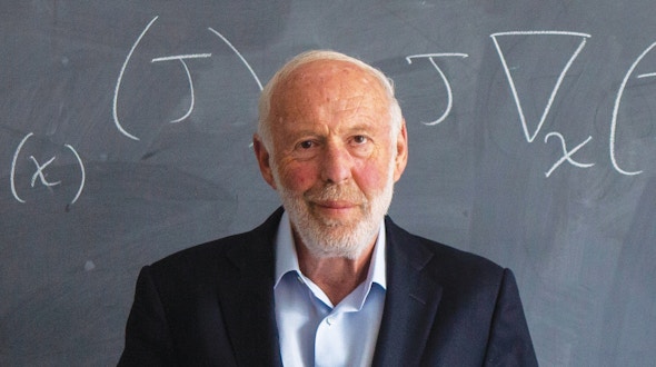 Jim Simons stands in front of a chalkboard. A mathematical equation is written on the board.